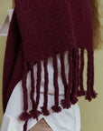 Detail des Alpaka-Oversize-Schals Gabriela in Berry mit grober Strickstruktur und langen geknoteten Fransen.