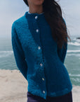 Nahaufnahme der türkisen Bouclé-Strickjacke Cruz mit Stehkragen, hellen Knöpfen und weicher Bouclé-Struktur.