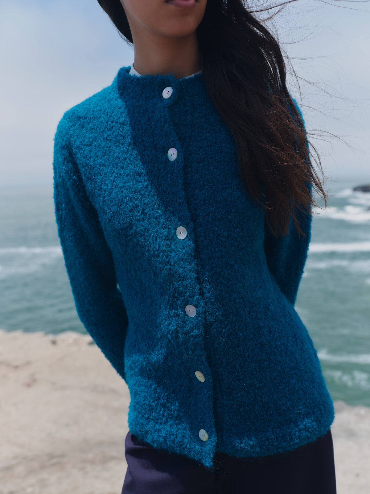 Nahaufnahme der türkisen Bouclé-Strickjacke Cruz mit Stehkragen, hellen Knöpfen und weicher Bouclé-Struktur.