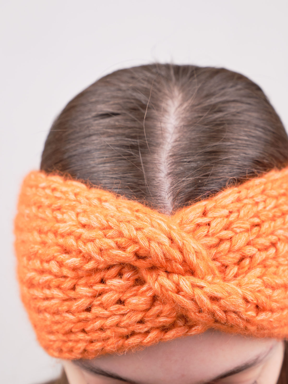 Alpaka-Stirnband Vero in Orange an einer Frau – Frontansicht der gedrehten Vorderseite.