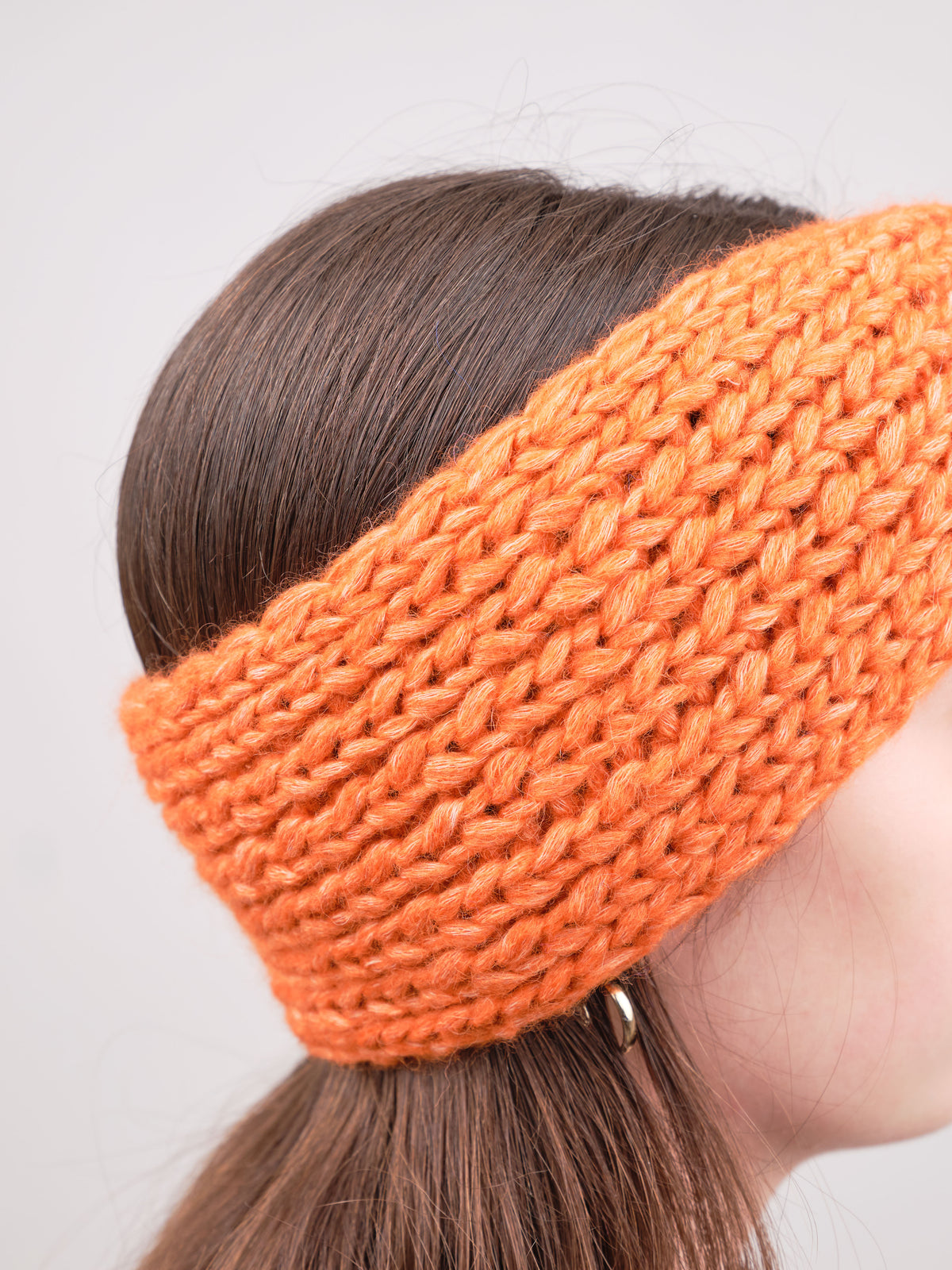 Alpaka-Stirnband Vero in Orange an einer Frau – seitliche Trageansicht mit sichtbarer Strickstruktur.