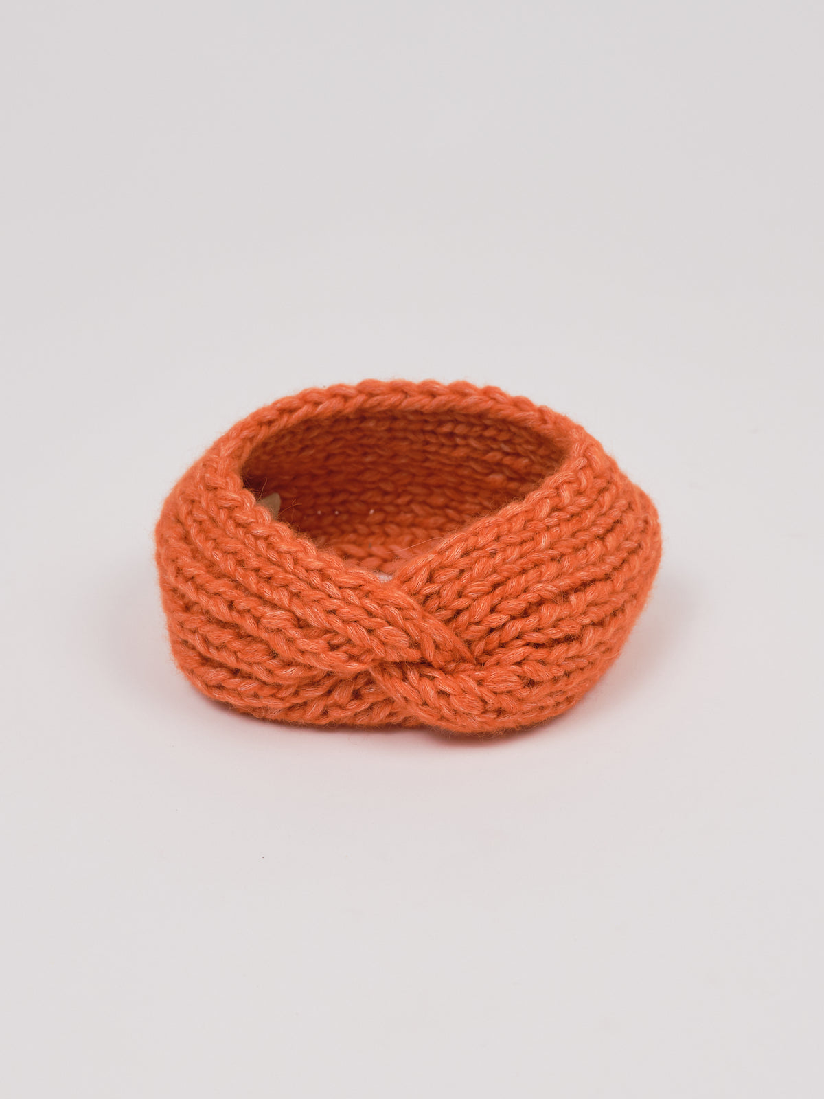 Gestricktes Stirnband in Orange von Manuela Bedford – aufgestellt mit gedrehter Vorderseite.