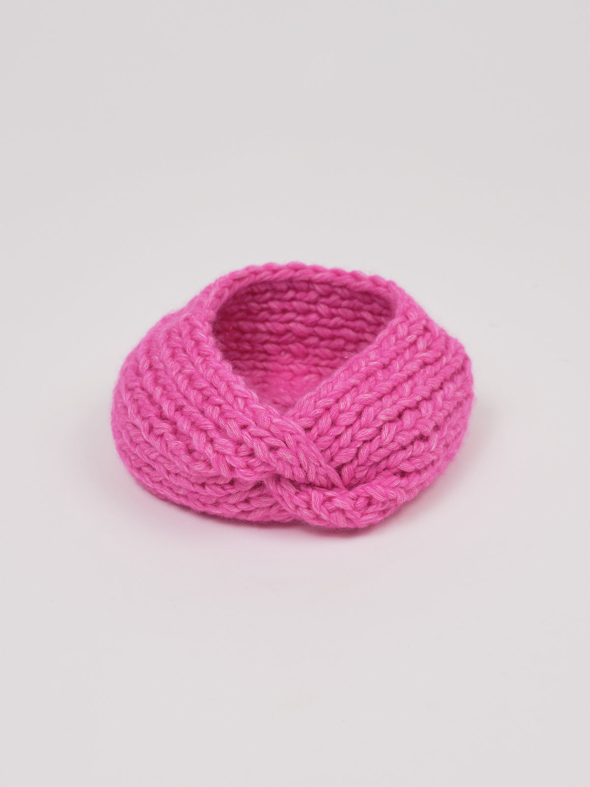 Gestricktes Stirnband in Pink von Manuela Bedford – aufgestellt mit gedrehter Vorderseite.